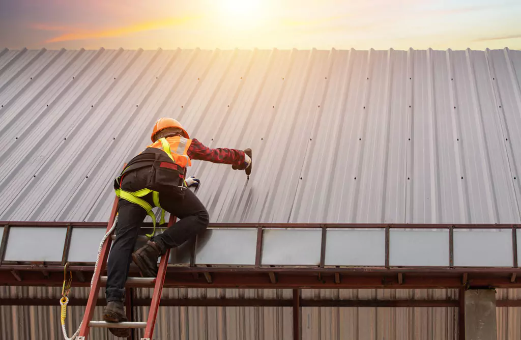 A Worker Fixing Metal Siding on a Building During Sunset